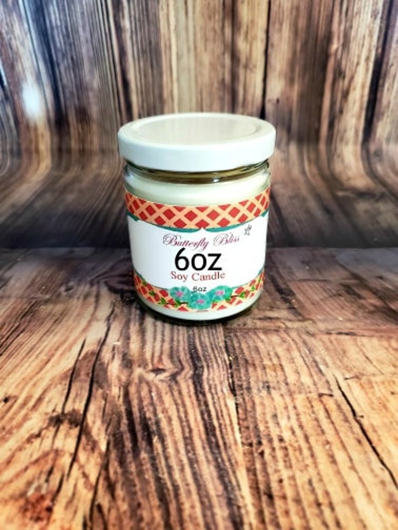 May include: A 6 oz soy candle in a clear glass jar with a white lid. The jar has a red, white, and blue patterned label with the text "Butterfly Bliss 6 oz Soy Candle".