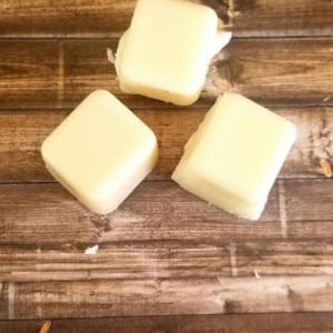 May include: Three square-shaped, white, solid, wax blocks on a brown wooden surface.
