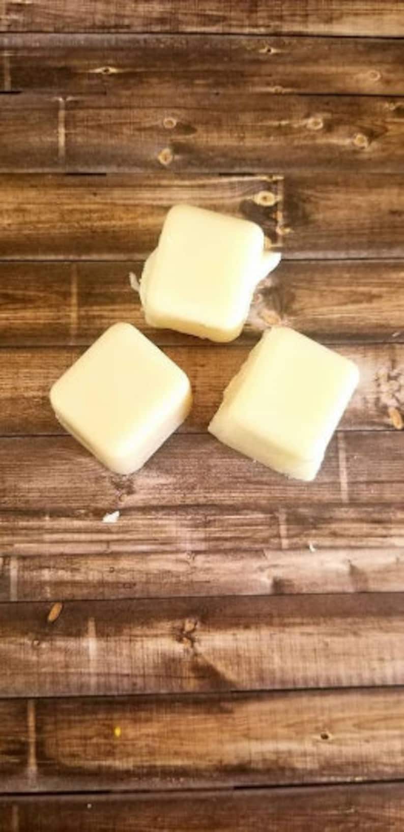 May include: Three square-shaped, white, solid, wax blocks on a brown wooden surface.