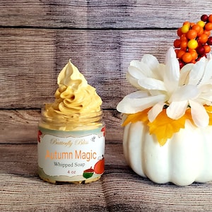 May include: A 4 ounce jar of whipped soap labeled "Butterfly Bliss Autumn Magic Whipped Soap". The soap is a light orange color and is topped with a swirl of whipped soap. The jar is sitting on a wooden surface with a white pumpkin and a sprig of fall-colored berries in the background.