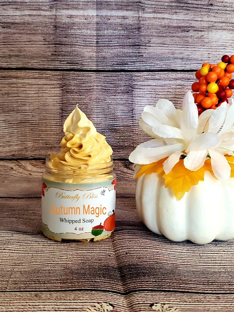 May include: A 4 ounce jar of whipped soap labeled "Butterfly Bliss Autumn Magic Whipped Soap". The soap is a light orange color and is topped with a swirl of whipped soap. The jar is sitting on a wooden surface with a white pumpkin and a sprig of fall-colored berries in the background.