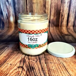 K&ouml;nnte beinhalten: Eine 16 Unzen Sojawachskerze in einem durchsichtigen Glasgef&auml;&szlig; mit einem rot-wei&szlig;-blauen Etikett, auf dem "Butterfly Bliss" und "Soy Candle" steht.
