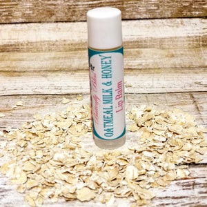 May include: A white tube of lip balm with a turquoise and pink label that reads "Butterfly Bliss Oatmeal Milk & Honey Lip Balm". The tube is sitting on a pile of oatmeal flakes.