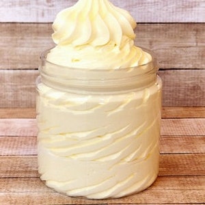 May include: A white whipped body butter in a clear glass jar with a screw-on lid. The jar is sitting on a wooden surface.
