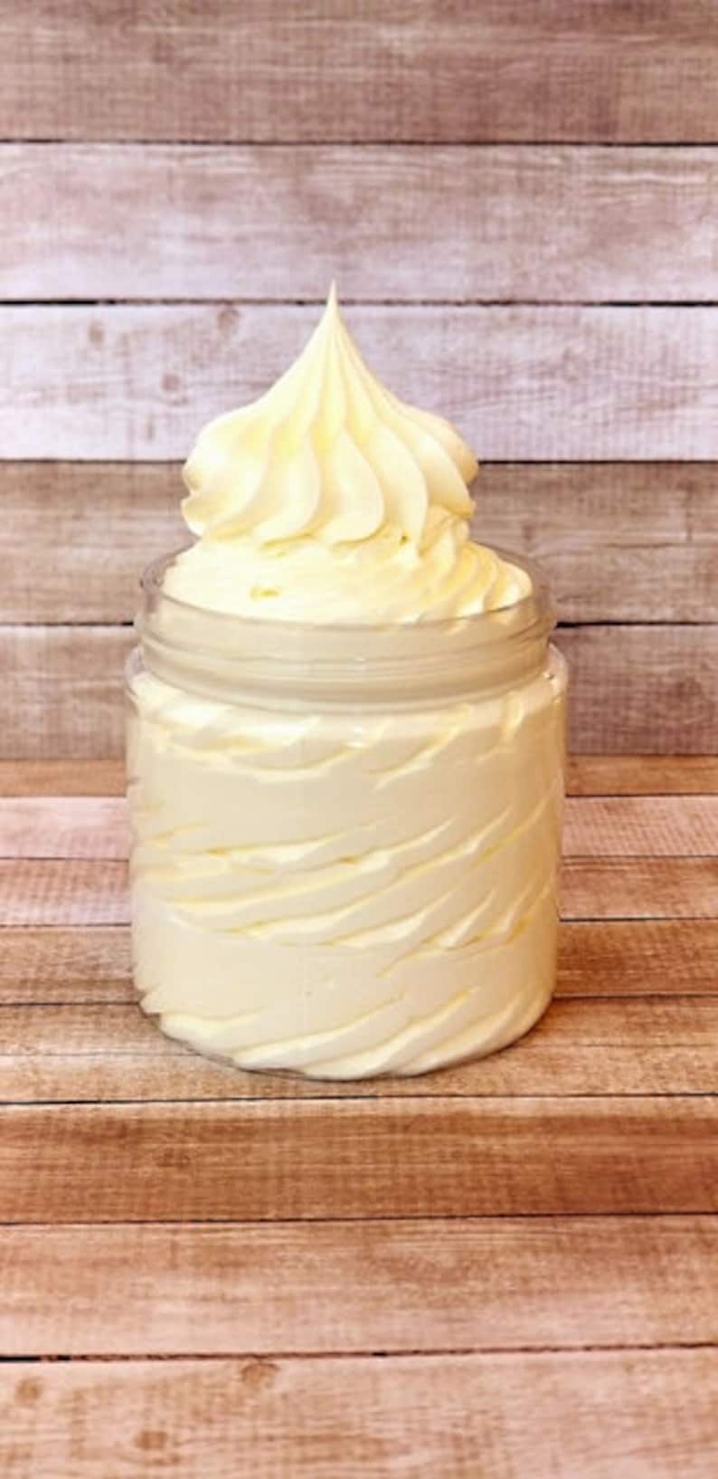 May include: A white whipped body butter in a clear glass jar with a screw-on lid. The jar is sitting on a wooden surface.