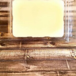 May include: A clear plastic container with a rectangular block of yellow wax inside. The container is sitting on a wooden surface.