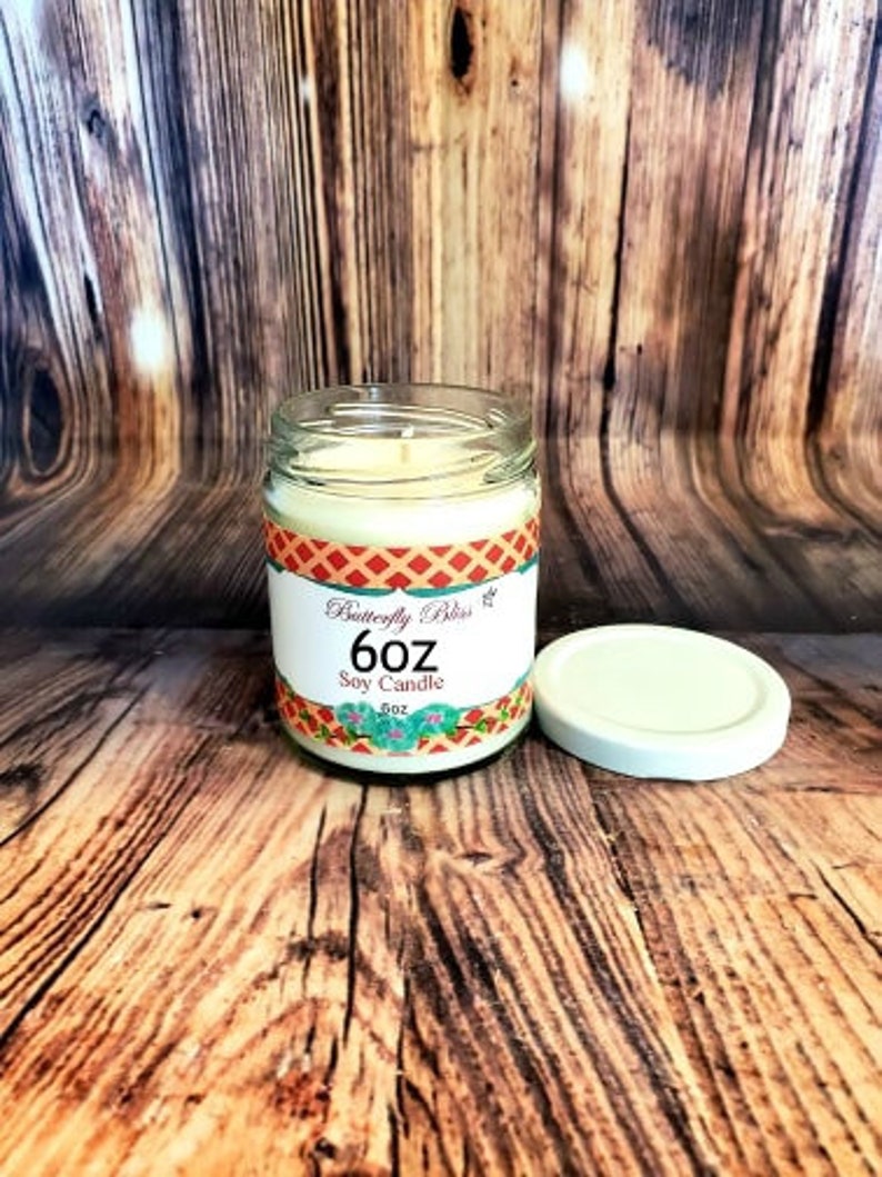 May include: A 6 oz soy candle in a clear glass jar with a colorful label that says "Butterfly Bliss 6 oz Soy Candle".