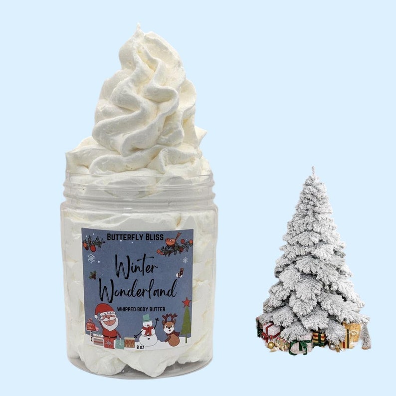 May include: A white whipped body butter in a clear jar with a label that reads "Butterfly Bliss Winter Wonderland Whipped Body Butter 8 oz". The jar is sitting in front of a small white flocked Christmas tree with presents at the base.