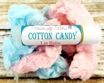 May include: A white lip balm tube with a blue and gold label that reads "Butterfly Bliss Cotton Candy Lip Balm". The tube is surrounded by pink and blue cotton candy.