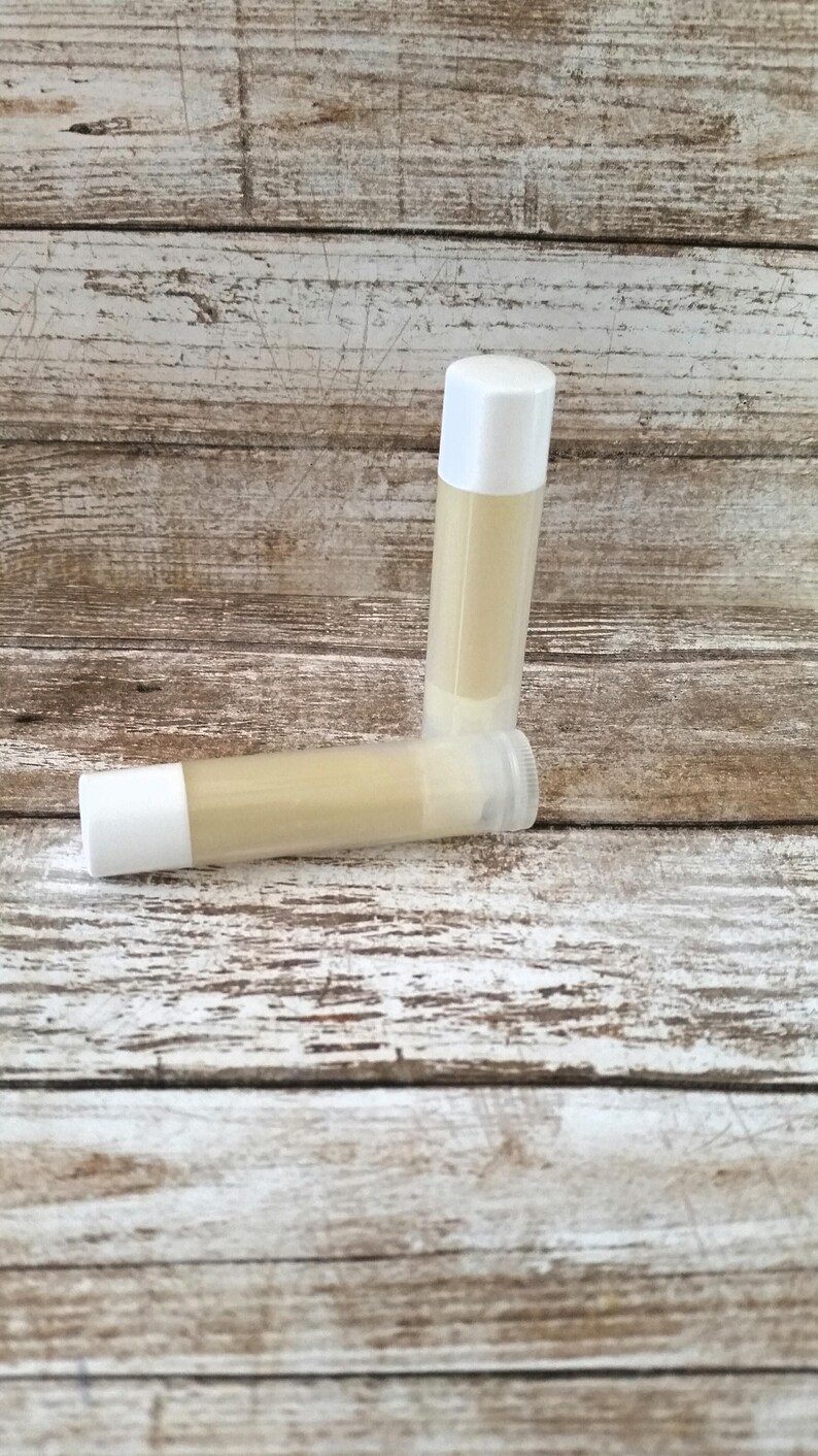 May include: Two white tubes of lip balm, one lying on its side and the other standing upright. The lip balm is a light yellow color.