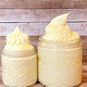 May include: Two jars of whipped body butter, one larger than the other, both with a swirl design. The jars are on a wooden surface.