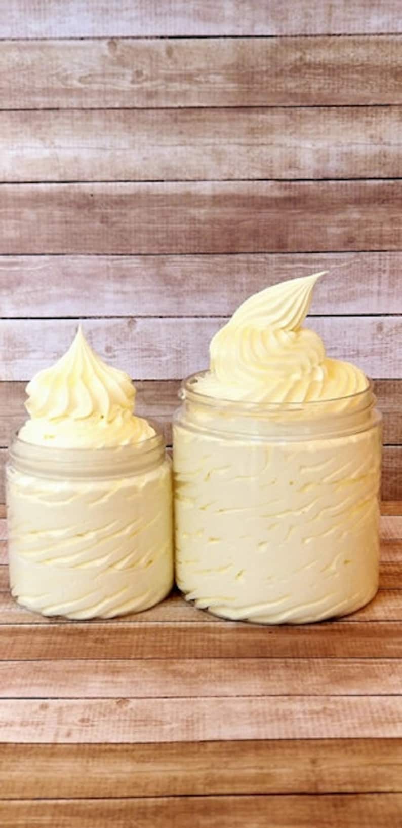 May include: Two jars of whipped body butter, one larger than the other, both with a swirl design. The jars are on a wooden surface.