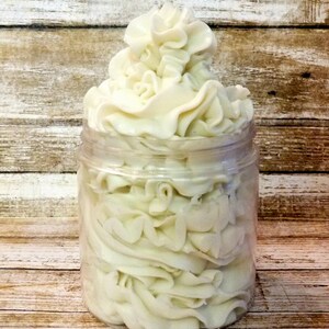 May include: A clear glass jar filled with a white whipped body butter. The butter is piled high and has a smooth, creamy texture.