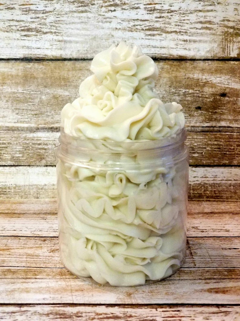 May include: A clear glass jar filled with a white whipped body butter. The butter is piled high and has a smooth, creamy texture.