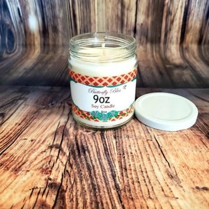 May include: A 9 oz soy candle in a clear glass jar with a red, white, and blue patterned label. The label reads "Butterfly Bliss" and "Soy Candle".