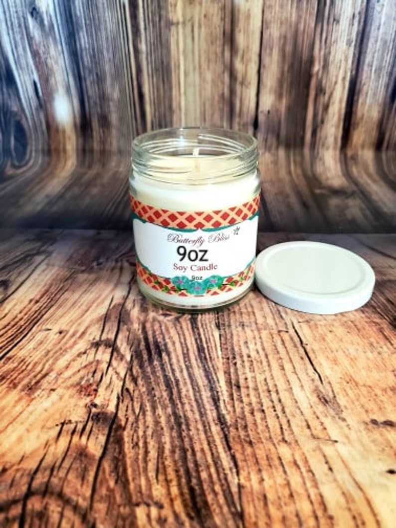 May include: A 9 oz soy candle in a clear glass jar with a red, white, and blue patterned label. The label reads "Butterfly Bliss" and "Soy Candle".