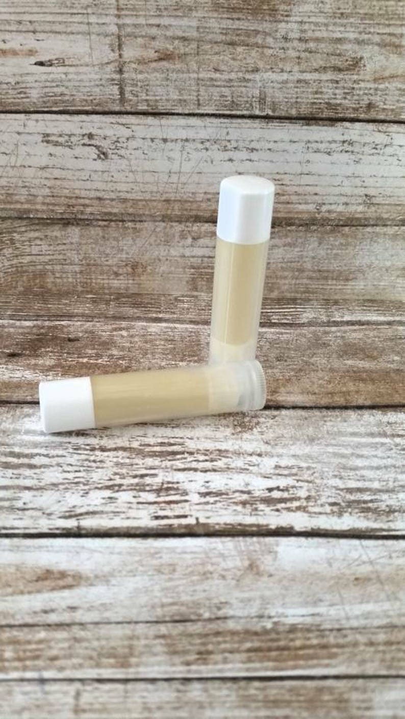 May include: Two white tubes of lip balm on a wooden surface. The lip balm is a light yellow color.