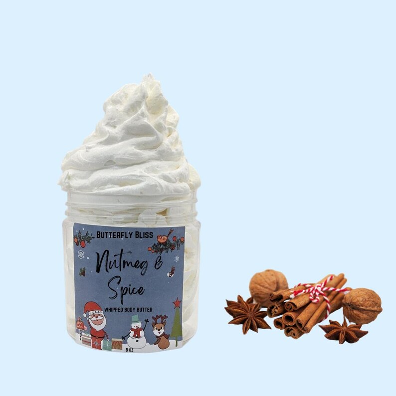 May include: A white whipped body butter in a clear jar with a blue and white label that says "Butterfly Bliss Nutmeg & Spice Whipped Body Butter 8 oz". The jar is sitting on a light blue background. There are cinnamon sticks, star anise, and walnuts in the lower right corner of the image.