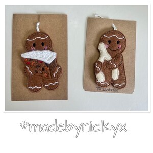 May include: Two brown felt gingerbread person ornaments attached to brown cardstock. One holds a slice of pie with white frosting, and the other holds a white wishbone. Both have embroidered facial features and white icing details. Text reads #madebynickyx.