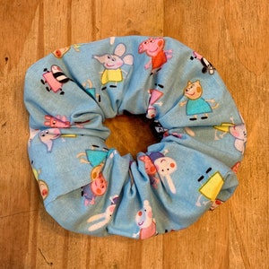 May include: A blue fabric scrunchie with a cartoon character print. The characters are pink pigs, a mouse, and a yellow duck.