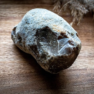 May include: A dark gray flint stone with a rough, textured surface. The stone has a sharp edge and appears to be a prehistoric tool.