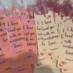 May include: A collection of pink and white bookmarks with the text "I have loved you with an everlasting love" in elegant calligraphy. Each bookmark features a small floral design and the reference "Jeremiah 31:3". Ribbons are attached.