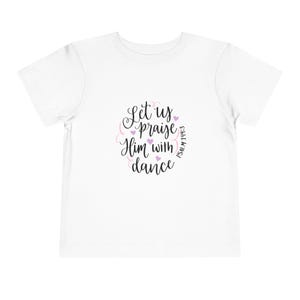 Op de afbeelding: Een wit T-shirt met korte mouwen en zwarte cursieve tekst die Let us praise Him with dance en Psalm 149:3 leest. Het ontwerp is versierd met kleine lichtpaarse hartjes en dunne roze krullende lijnen in het midden op de voorkant.