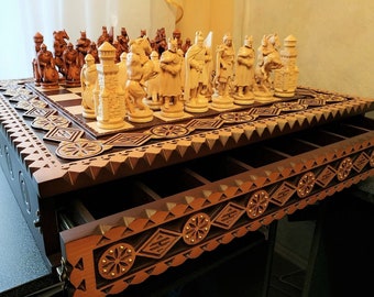 May include: A wooden chess set with intricately carved pieces and a storage drawer. The chessboard is made of dark wood with light squares and features a decorative border. The pieces are made of light wood and are detailed with carvings.