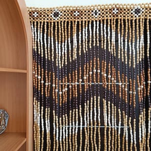 Könnte beinhalten: Ein Vorhang aus Holzperlen mit braunen, weißen und naturfarbenen Perlen. Die Perlen sind in einem geometrischen Muster angeordnet.