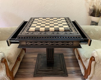 May include: A wooden chess table with intricate carvings and two drawers. The table has a black and white checkered playing surface and a dark brown finish.