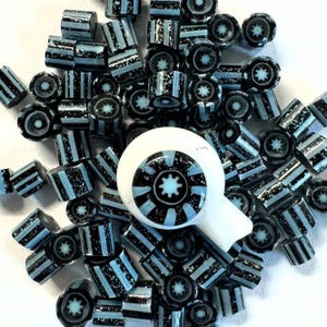 May include: A collection of black and light blue striped glass beads and a white glass eye with a black and light blue starburst design. The beads are cylindrical and have a speckled appearance.
