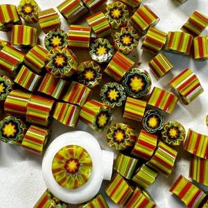 Puede incluir: Una colección de cuentas de vidrio de colores con un patrón a rayas y floral. Las cuentas son rojas, amarillas y verdes.