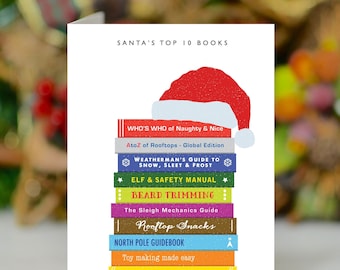 May include: A Christmas-themed greeting card featuring a stack of colorful books topped with a Santa hat. The books have titles like "Who's Who of Naughty & Nice" and "Beard Trimming". The text "SANTA'S TOP 10 BOOKS" is at the top.