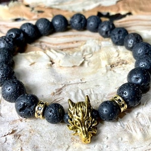 May include: Black lava rock beaded bracelet with a gold wolf head charm. The bracelet is made of natural lava rock beads and features a detailed gold wolf head charm.
