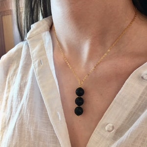 May include: A gold chain necklace with three black lava rock beads hanging from it.