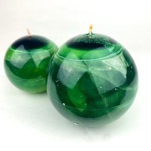 May include: Two green sphere candles with a white swirl design. The candles have a black center and a small wick.