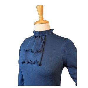 Pode incluir: Um suéter azul marinho de manga comprida com gola de babados e um padrão de bolinhas.