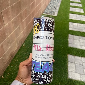 May include: A black and white stainless steel tumbler with a notebook paper design. The tumbler has the text "COMPOSITION BOOK" and "Ms. Reese" on it. The tumbler also has the text "100 Sheets 200 Pages 9 3/4 x 7 1/2 in / 24.7 x 19.0 cm" on it. The tumbler has the word "TEACHER" in purple and blue letters on the bottom.