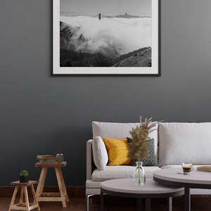 Black and white photograph of the Golden Gate Bridge sinking into fog, shot on 4x5 film, shown as a framed print hanging in a furnished room