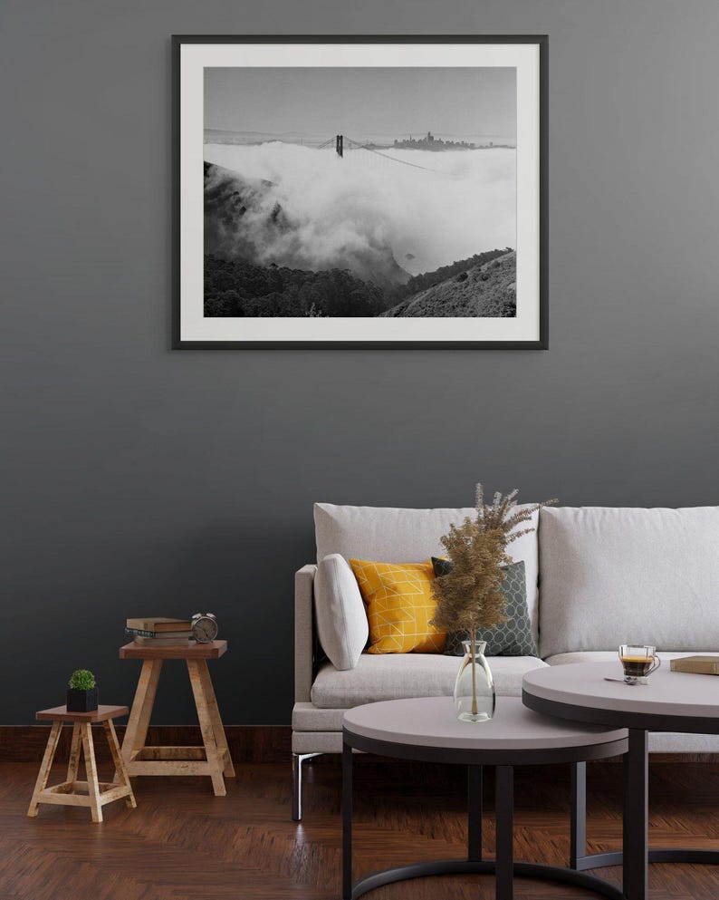 Black and white photograph of the Golden Gate Bridge sinking into fog, shot on 4x5 film, shown as a framed print hanging in a furnished room