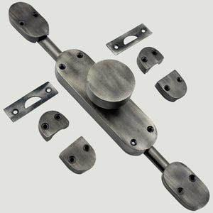 Op de afbeelding: Een set deurbeslag van donkergrijs metaal met een centrale ronde knop op een langwerpige ovale plaat, twee bijpassende eindkappen, twee kleine rechthoekige sluitplaten en vier halfronde montagebeugels met voorgeboorde gaten.