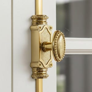 May include: A brass-coloured door latch with an oval handle and decorative detailing. The latch is mounted on a white door and features a textured surface and cross-shaped screws. The hardware is designed for doors and windows.