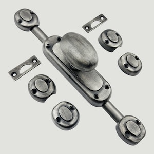 Könnte beinhalten: Ein dunkelgrauer Fensterriegel aus Metall mit einem ovalen Griff auf einer zentralen Platte, begleitet von zwei rechteckigen Schließblechen und vier kleinen runden Montagehalterungen, alle mit einer verwitterten, texturierten Oberfläche.