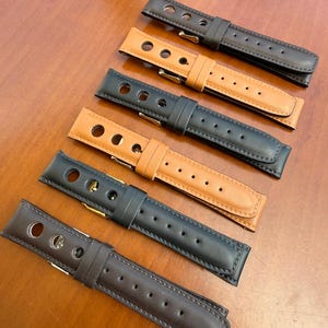 Könnte beinhalten: Sechs Leder-Uhrenarmbänder in verschiedenen Farben, darunter Schwarz, Braun und Beige. Jedes Armband hat eine kontrastierende Unterseite und eine Metallschnalle. Die Armbänder haben mehrere Löcher zur Anpassung und sind für eine Uhr konzipiert.