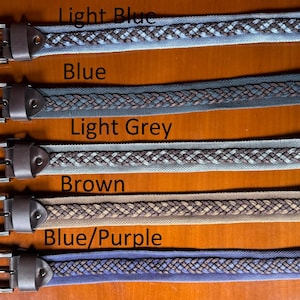 Puede incluir: Cinco cinturones trenzados en diferentes colores, incluyendo azul claro, azul, gris claro, marrón y azul/morado. Cada cinturón tiene una hebilla de cuero marrón y un diseño tejido.