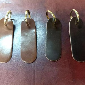 Può includere: Quattro portachiavi in ​​pelle con anelli in ottone. I portachiavi sono di colore marrone, marrone scuro, nero e marrone scuro. I portachiavi sono tutti della stessa dimensione e forma.