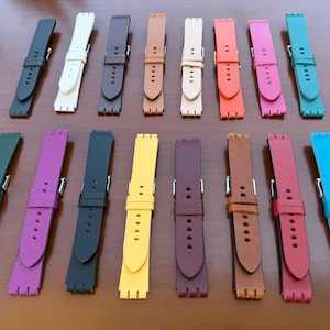 Könnte beinhalten: Eine Sammlung farbenfroher Uhrenarmbänder in verschiedenen Farbtönen, darunter Schwarz, Weiß, Braun, Beige, Orange, Rosa, Türkis, Grün, Lila, Gelb, Burgunderrot und Rot. Die Armbänder bestehen aus flexiblem Material und haben einen Schnallenverschluss.