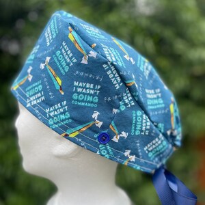 May include: Blue scrub hat with a white button and a repeating pattern of the phrase "Maybe if I wasn't going commando". The hat has blue ties.