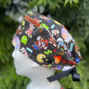 May include: Black scrub hat with a colorful print of various video game characters, including Mario, Pac-Man, and Donkey Kong. The hat has a black tie and the word "Progger" is visible on the hat.