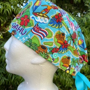 May include: A blue and green surgical scrub hat with a tropical print featuring palm trees, flowers, and the word "OAHU". The hat has a turquoise button and a light blue tie.